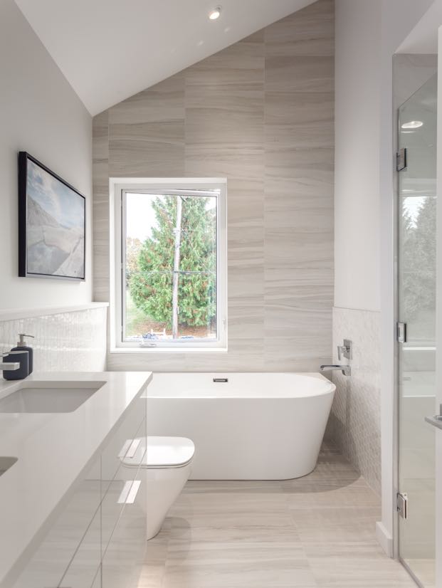 Interior image of a bathroom with the bath with serene sand colour tile walls featuring the window where you can see back yard.