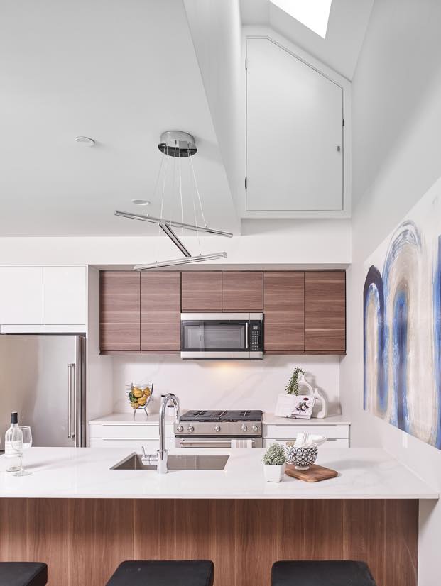 The interior image of the kitchen with timeless white and wood millwork design, featuring high ceiling, white marble kitchen island and artwork on the side wall, designed by N B A architects.