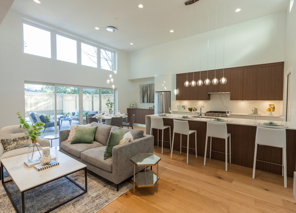 Interior image from the living room overlooking kitchen, timeless design with wooden millwork, white marble waterfall kitchen island and wide glass sliding doors and windows that provides lots of natural light and provides view to the interior yard.