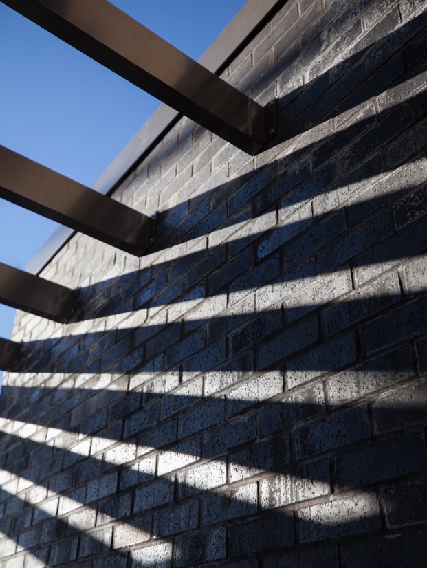 An exterior image featuring the modern entrance canopy and the shadows on black brick wall.