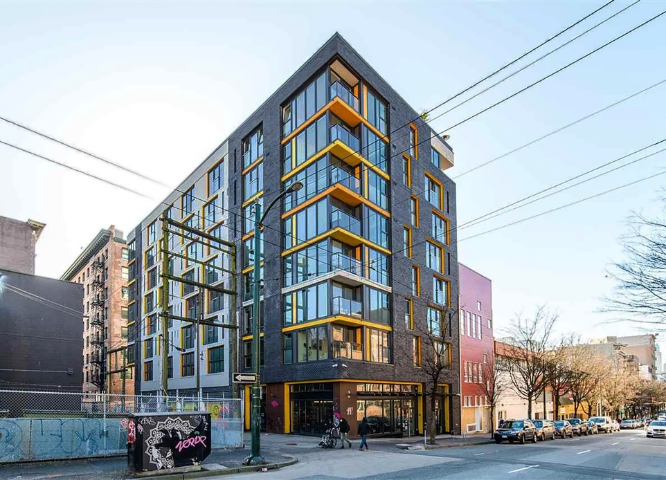 The exterior image of completed 8 storey mixed-use building in historic Gastown, Vancouver, BC, designed by nba architects. The building is modern, innovative, space efficient and features black brick and yellow metal panel elements in the façade.