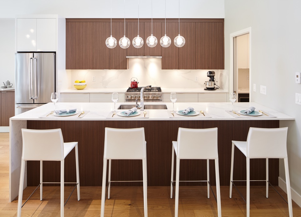 Interior image of the white and dark wood kitchen design and white marble waterfall kitchen island, featuring the modern lighting.
