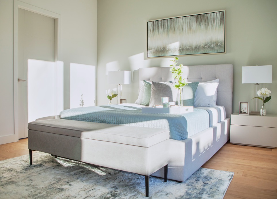 Interior image of a master bedroom featuring high ceilings and a cozy queen bed with white interior with light blue elements.