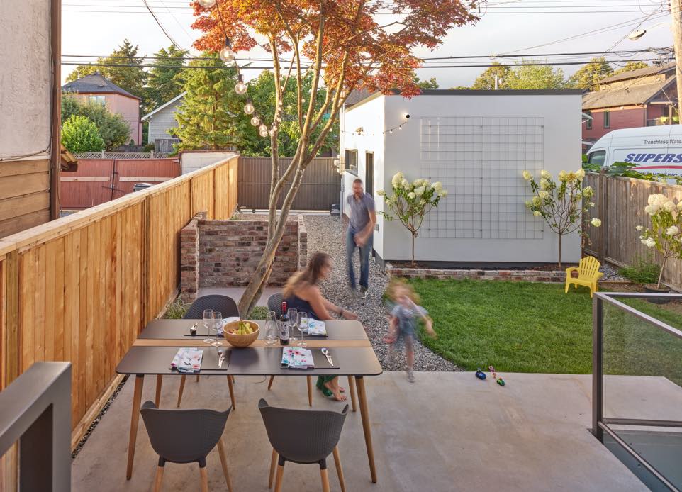 idyllic family image from the back yard of family playing and having a dinner. N B A architects designed the passive house with a detached garage building.