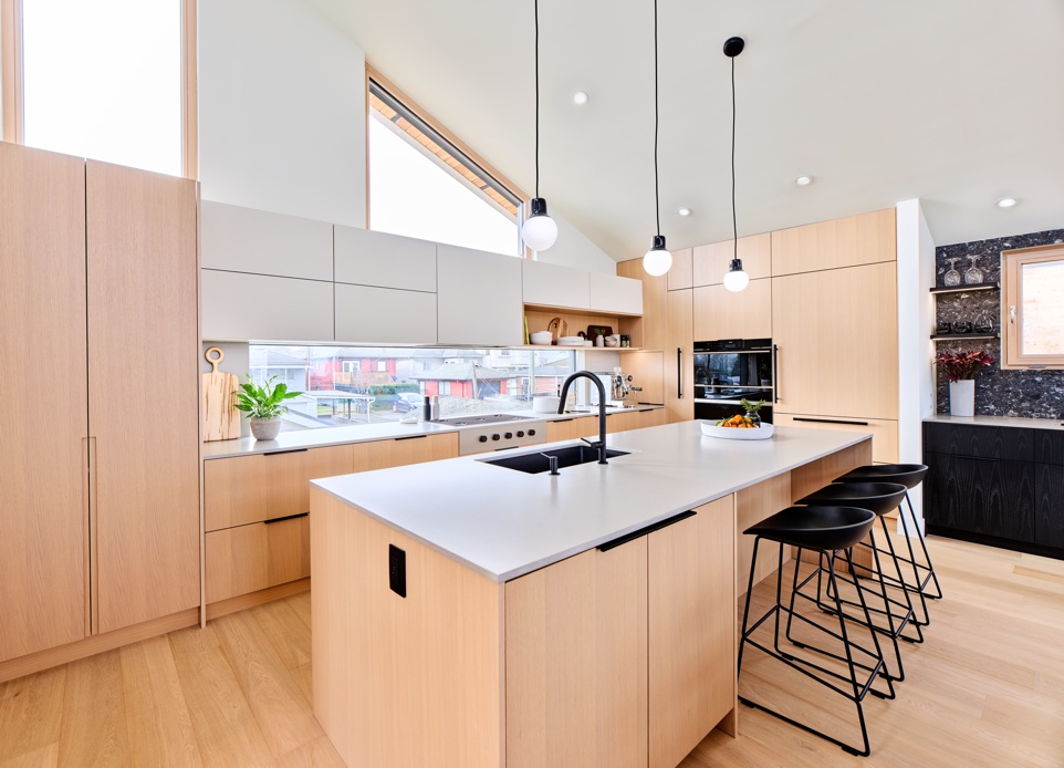 The interior image of kitchen featuring high ceiling and a white and light wood millwork with a modern wide kitchen island.