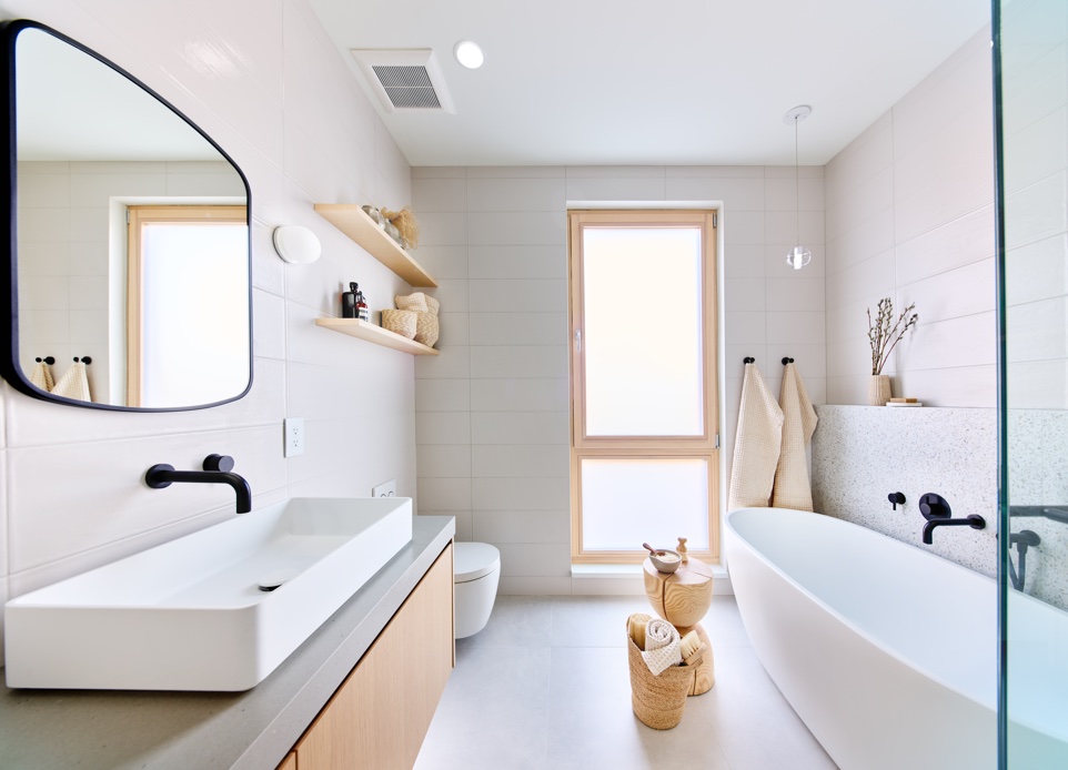 Interior image of a master bathroom with a free-standing bathtub and white tile walls featuring a large modern window that provides an abundance of natural light and privacy.