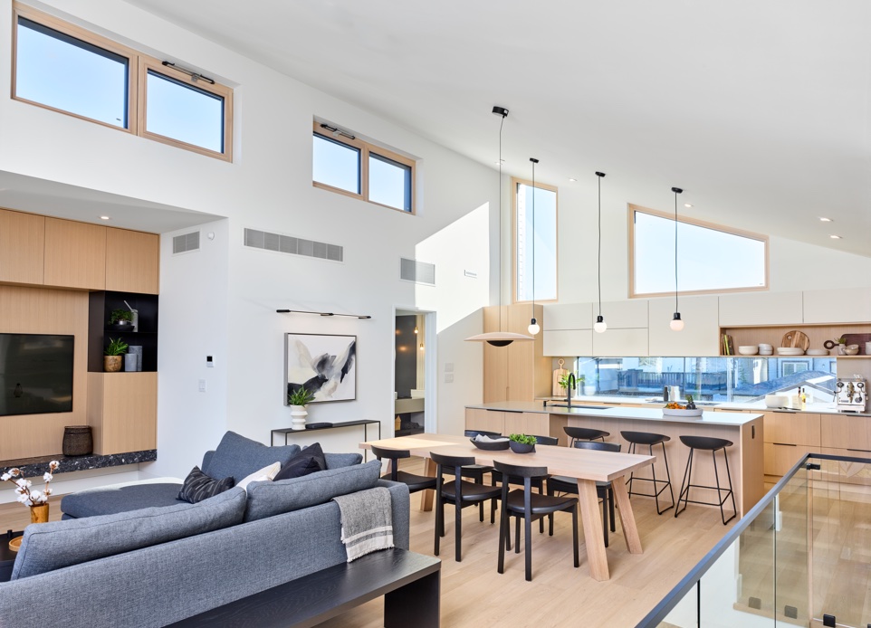 The interior image of the living, dining and kitchen spaces featuring high ceiling and a white and light wood millwork with a lot of natural light and a modern artwork.