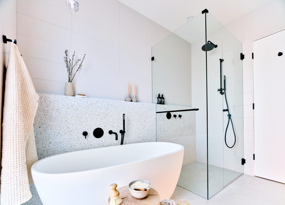 Interior image of a spacious master bathroom with a shower and a free-standing bathtub and white tile walls featuring high ceiling and modern black interior fixtures, timeless design by N B A architects.