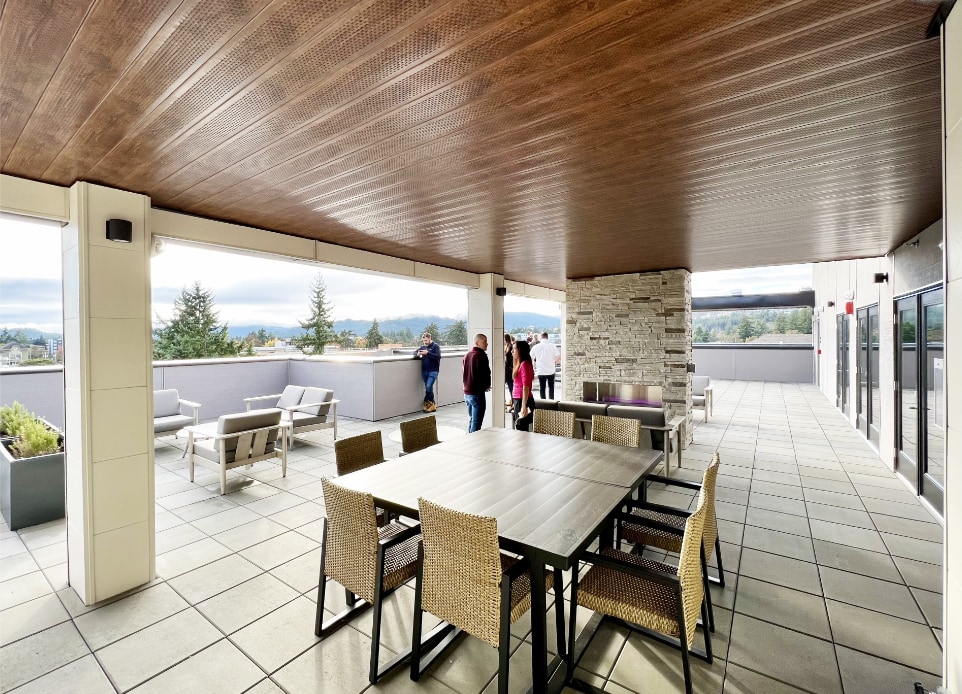 The exterior image of the roof top outdoor amenity space in a completed modern mid-rise, 6-stories strata apartment building above a podium car park ground parking in Langford, BC, designed by nba architects. Featuring rooftop resident amenity space opening onto a rooftop garden.