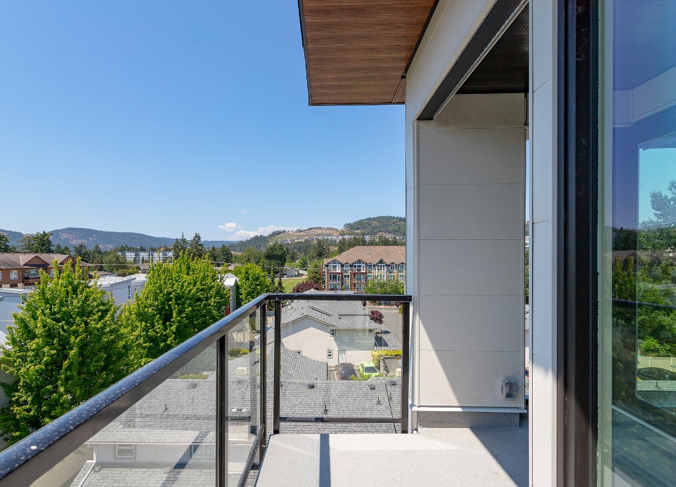 The exterior image of the 1 bed apartment balcony overlooking the mountain view in a completed modern mid-rise, 6-stories strata apartment building above a podium car park ground parking in Langford, BC, designed by nba architects. Featuring rooftop resident amenity space opening onto a rooftop garden.