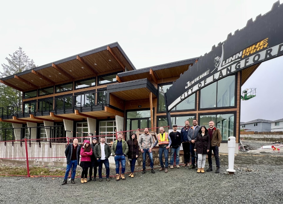 Exterior image of the completed clubhouse of the Jordie Lunn Bike Park featuring all the team that work on the design and building. Nba architects designed the building to be at one with the surrounding landscape, the facility contains community meeting spaces, washrooms/showers, a concession, and a bike repair / bike rental space. 