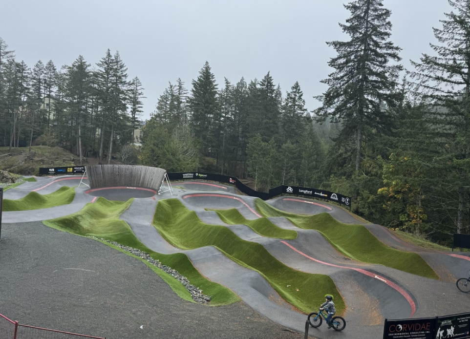 Exterior image of a bike park hills clubhouse of the Jordie Lunn Bike Park surrounded by trees. Nba architects designed the building to be at one with the surrounding landscape, the facility contains community meeting spaces, washrooms/showers, a concession, and a bike repair / bike rental space. 